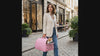 Woman carrying a cat in the pink Roam carrier, cat looking out the open top on a city street